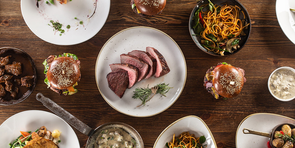 Gedeckter Tisch von Oben. Teller mit verschiedenen Gerichten. Fleisch und Pflanzliche.